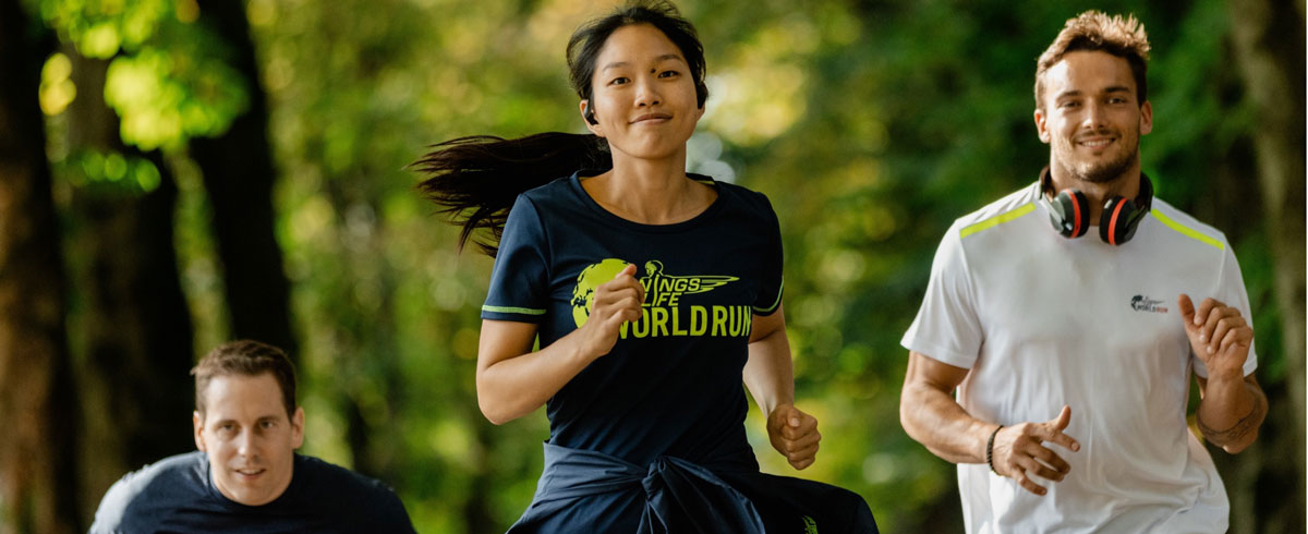 Drei Teilnehmer am Wings for Life World Run laufen mit einem Lachen auf dem Gesicht und tragen dabei Philips Sportkopfhörer.